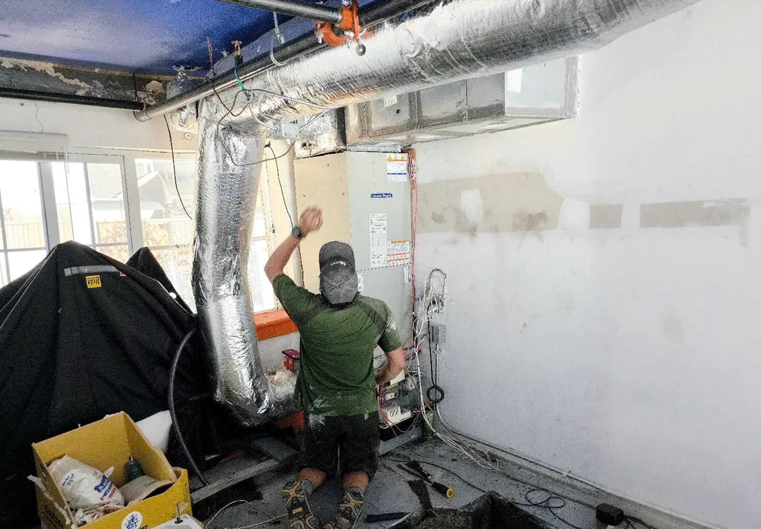 HVAC technician servicing a residential air handler and ductwork system during professional HVAC maintenance