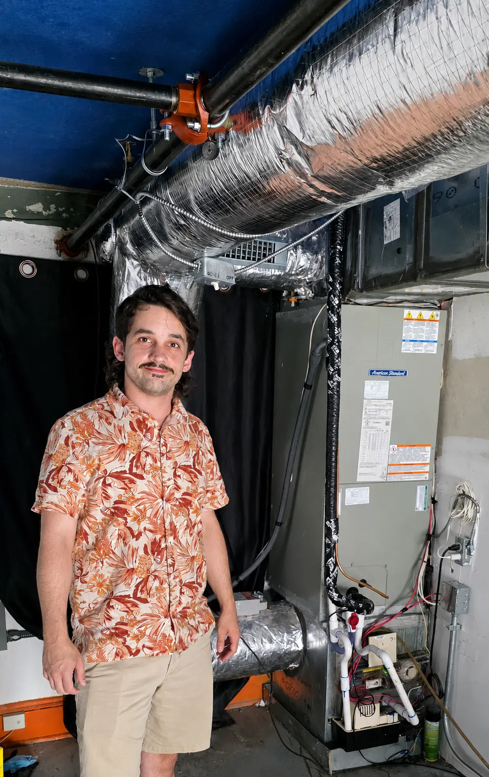 Residential HVAC technician standing beside a newly installed air handler and insulated ductwork system