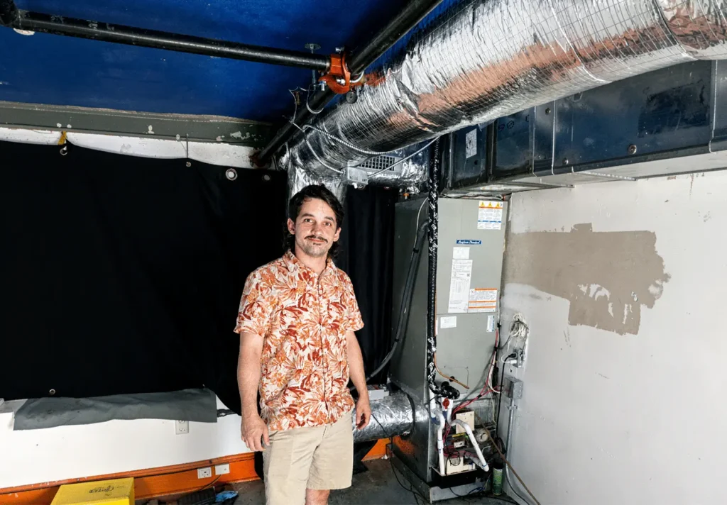 Residential HVAC technician standing beside a newly installed air handler and insulated ductwork system