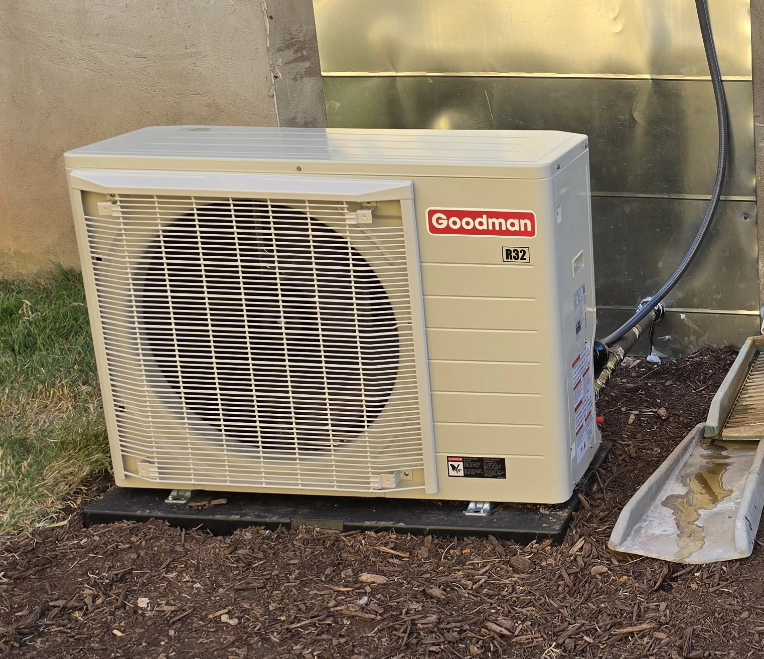 **Alt text:** Outdoor Goodman R32 air conditioning condenser unit installed beside a home as part of a residential HVAC system installation.
